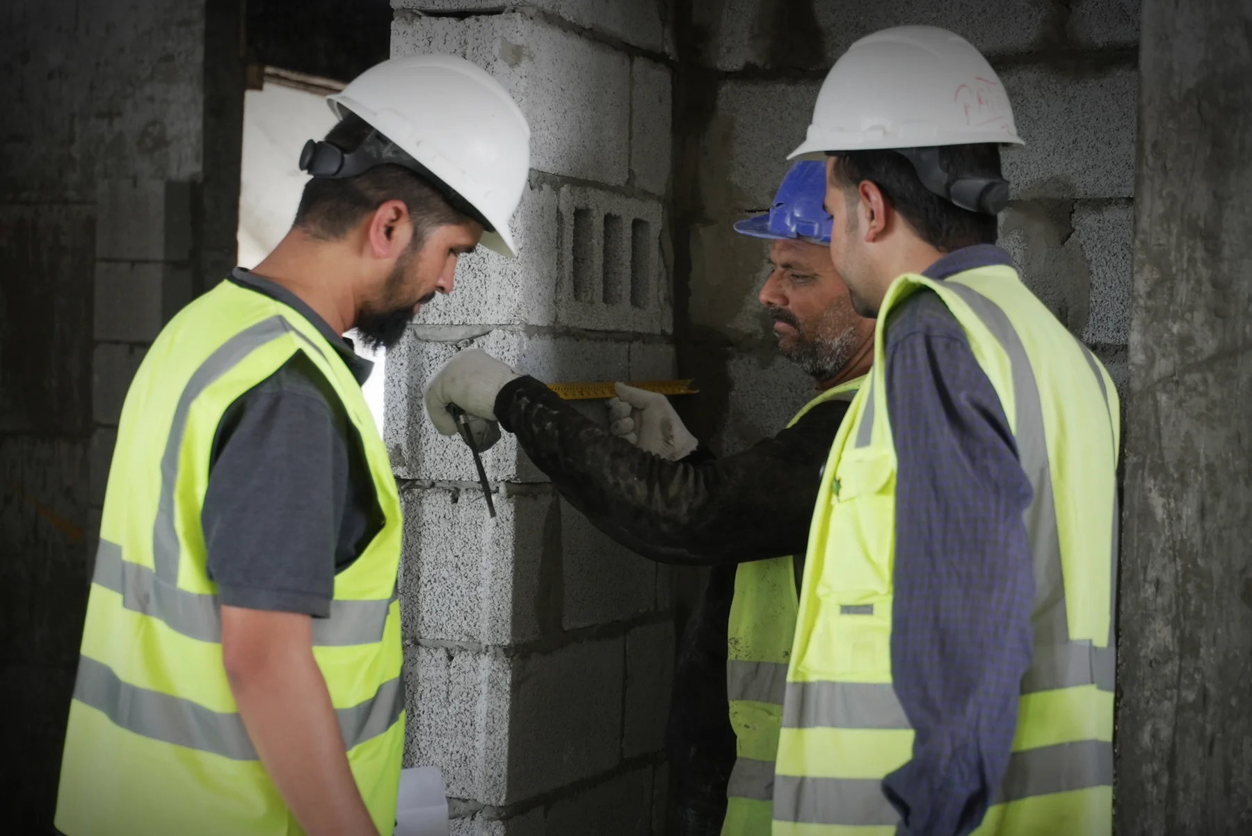 Builders in hard hats measuring a blockwork wall on site